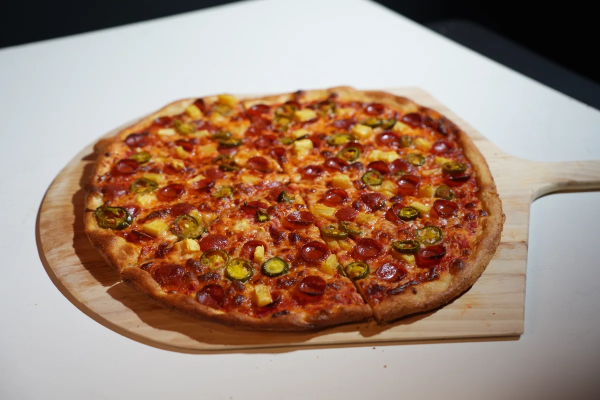 The Heretic Hawaiian pizza on a wooden pizza board